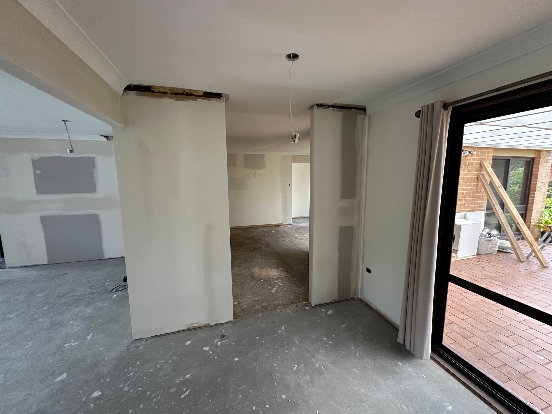 Partially renovated room with drywall, exposed floor, and an open doorway to a brick patio