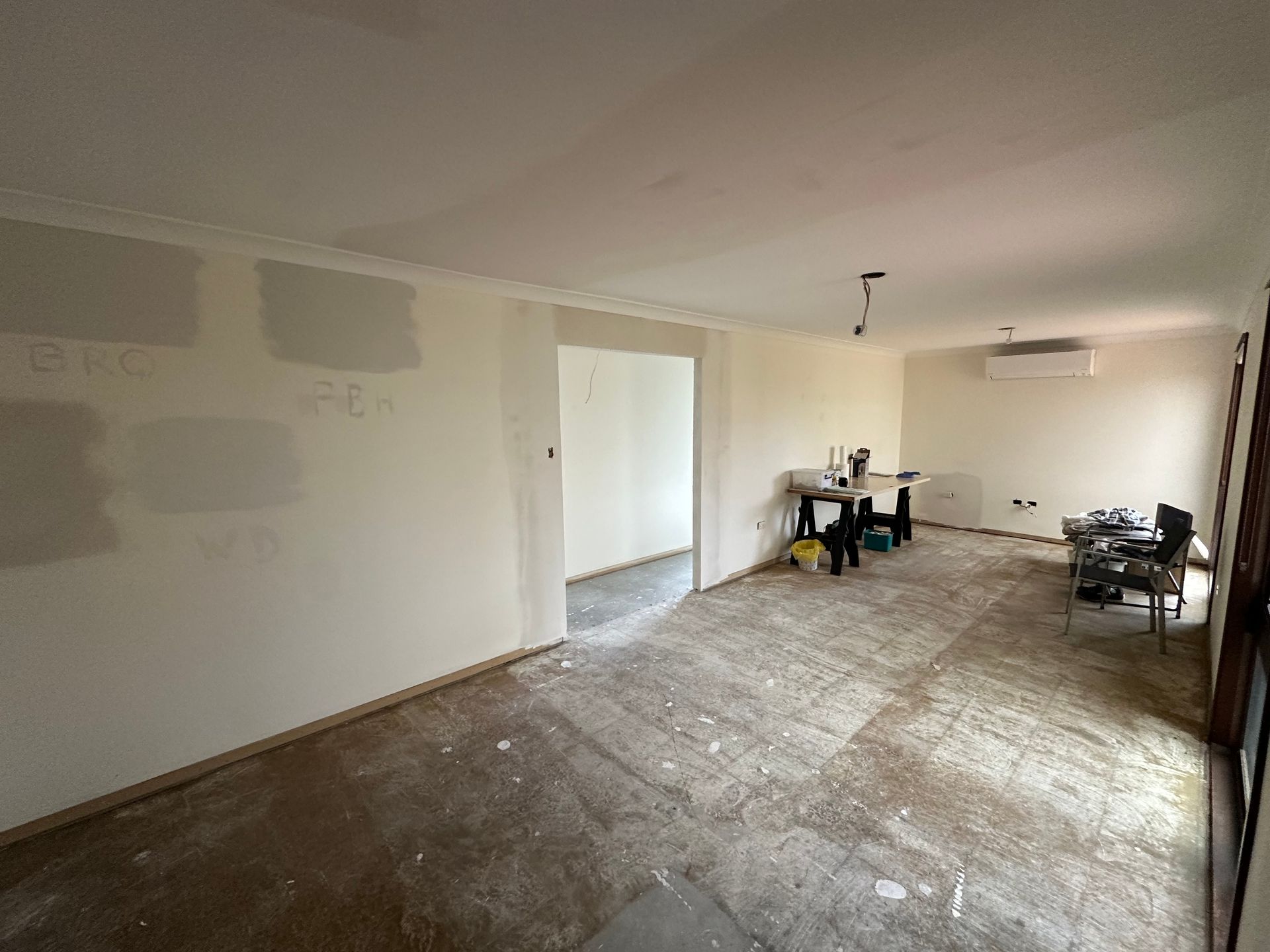 Empty unfinished room with bare walls, dusty floor, and a few chairs and tables near the back wall