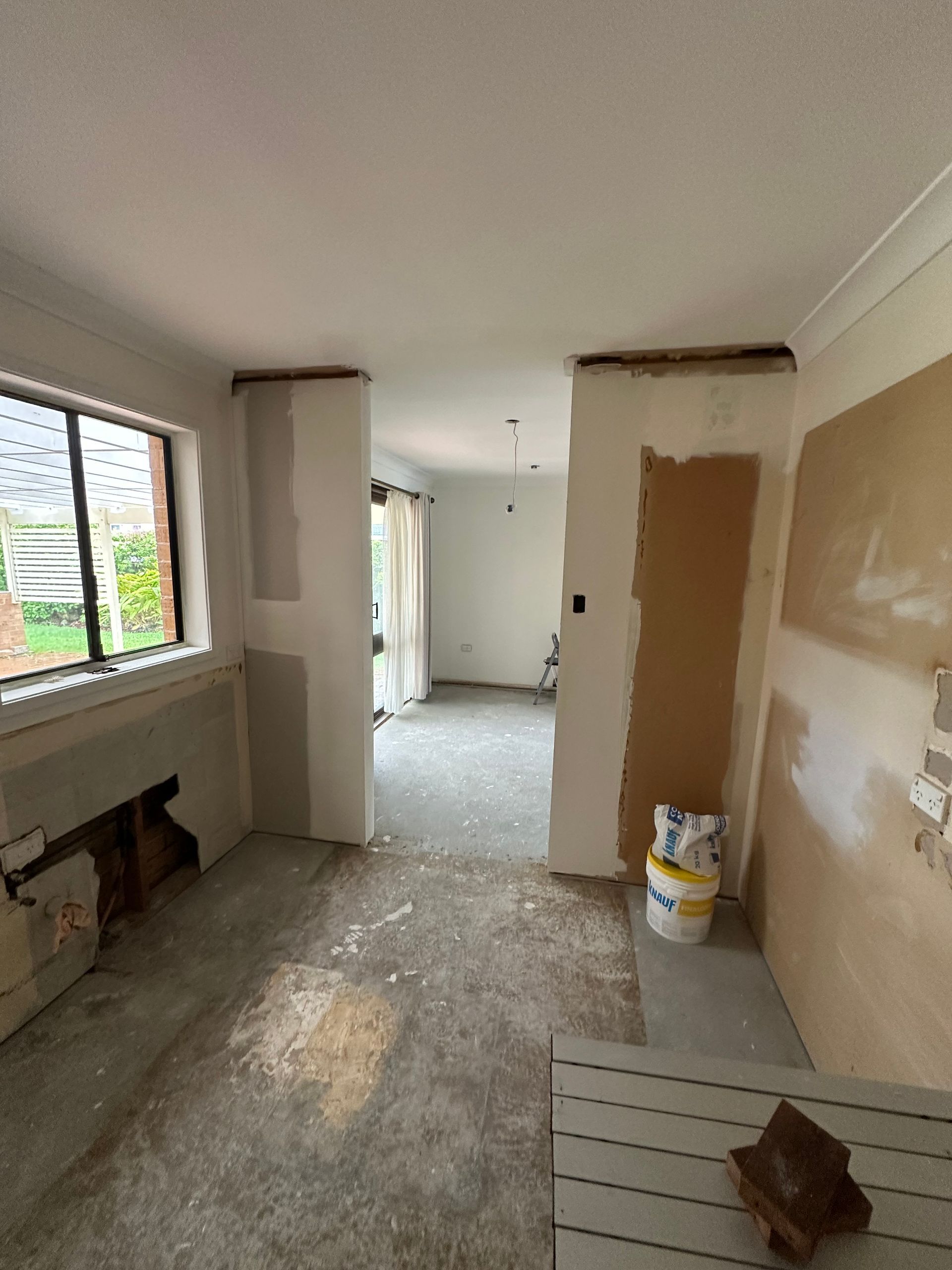 Partially renovated empty room with exposed walls, debris on floor, and a window on the left