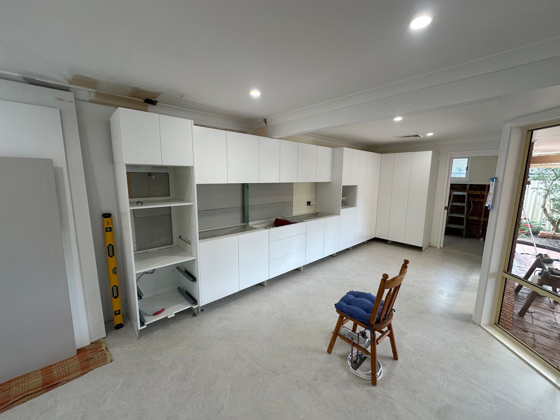 Bright empty room with white cabinets, tiled floor, and a chair near a glass door