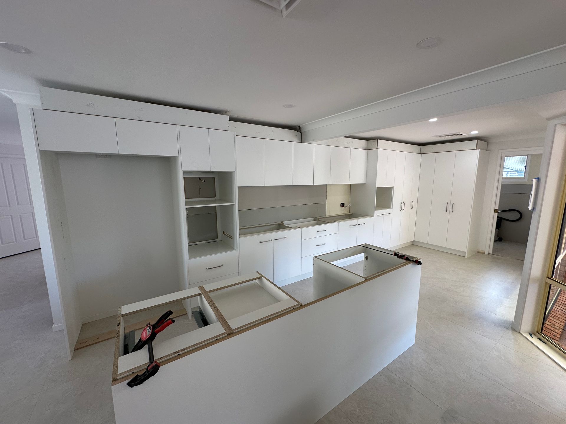 Bright white modern kitchen under renovation with unfinished island, cabinets, and exposed countertop openings