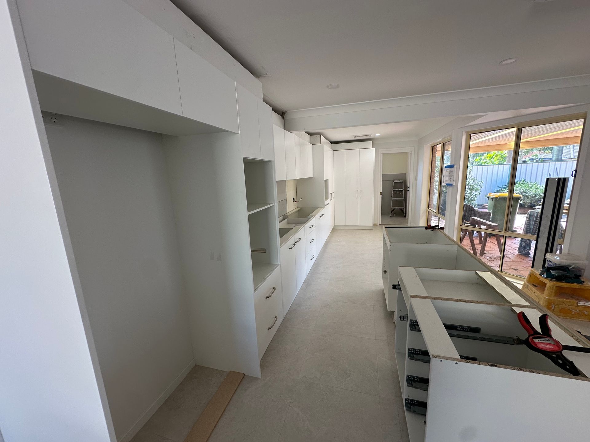 Modern white kitchen and living space with island, built-in cabinets, and large windows opening to a patio