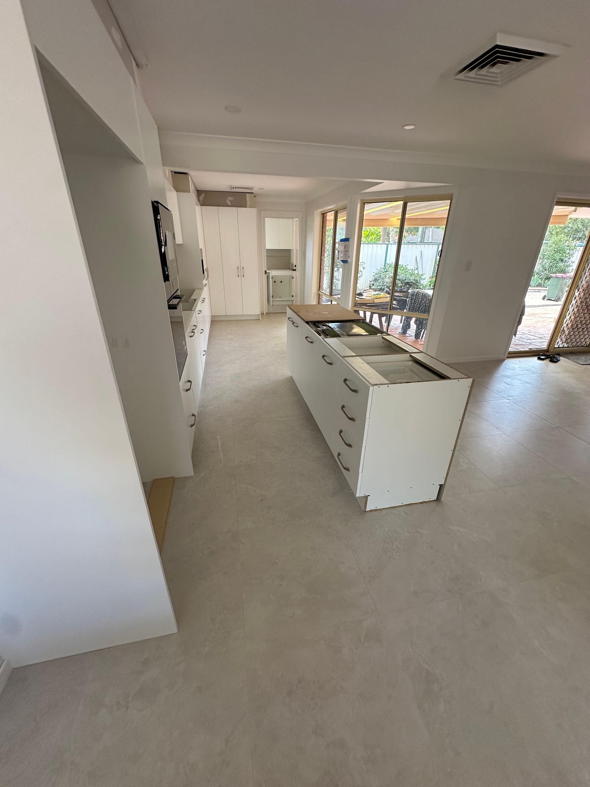 Empty modern kitchen with white island, light flooring, and large windows overlooking greenery.