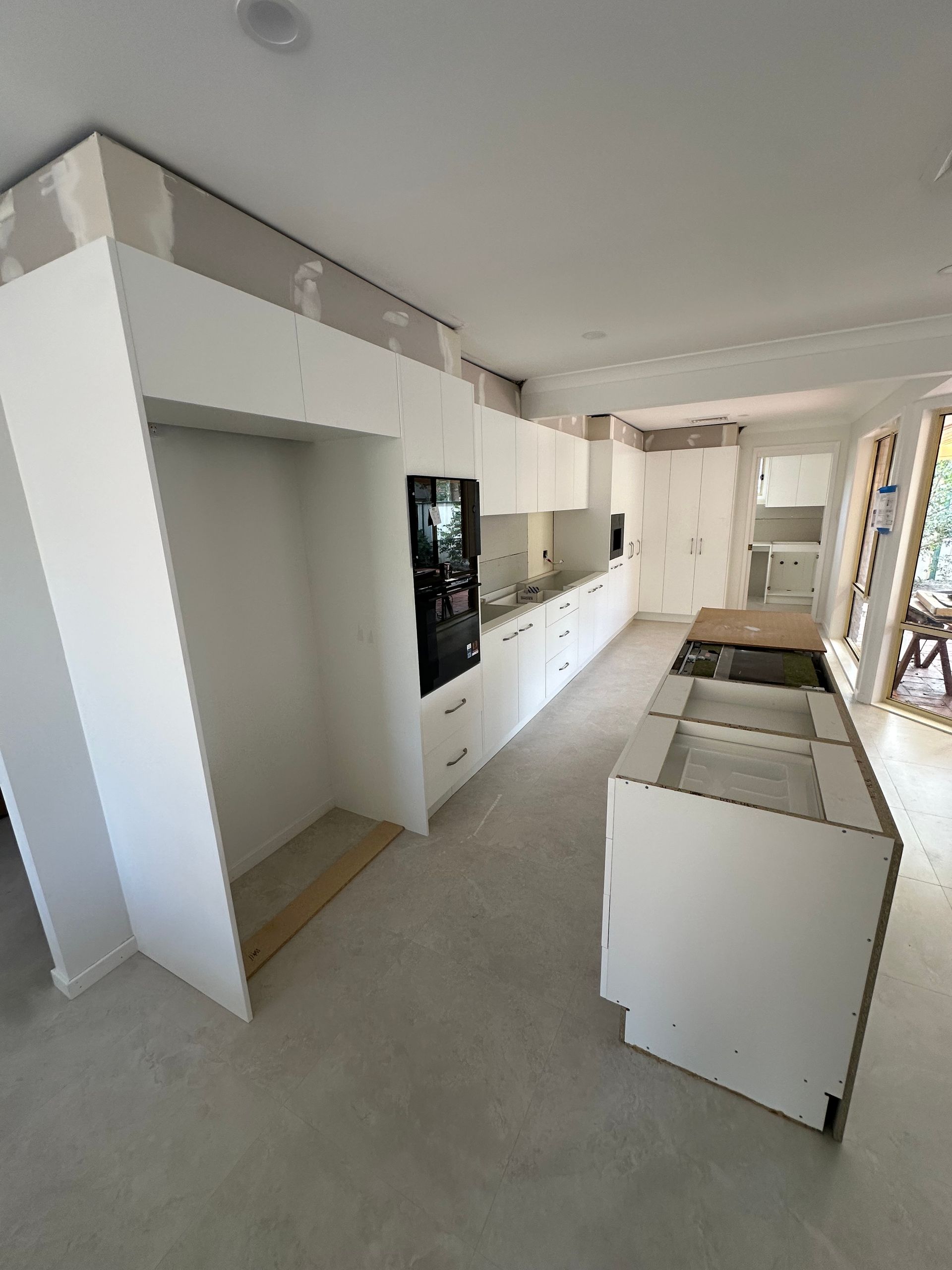 Empty modern kitchen with white cabinets, island, and bright windows in a long open-plan room