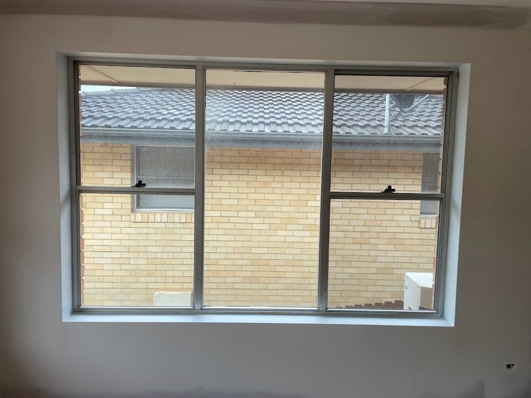 A view through a white-framed window looking out at a neighboring yellow brick house with a dark tiled roof.