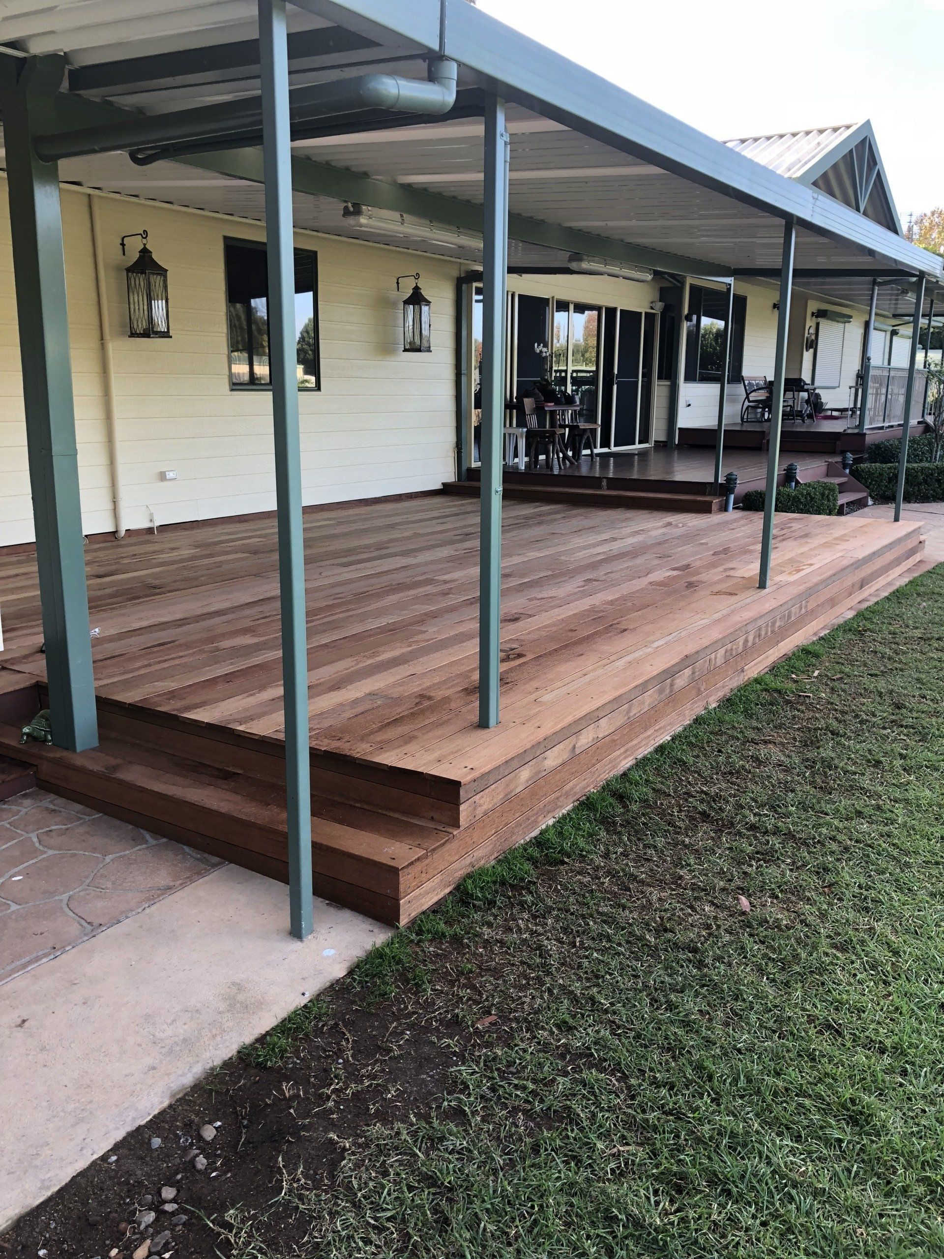 A large wooden deck with a covered patio area attached to the side of a house, featuring green structural posts.