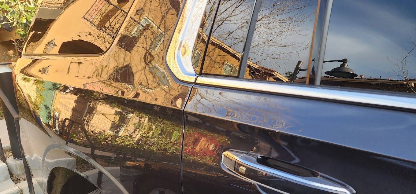 A black car is parked in a parking lot with a reflection of a building in the window.