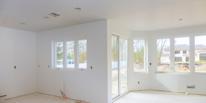 Empty white room under renovation with large windows and unfinished flooring