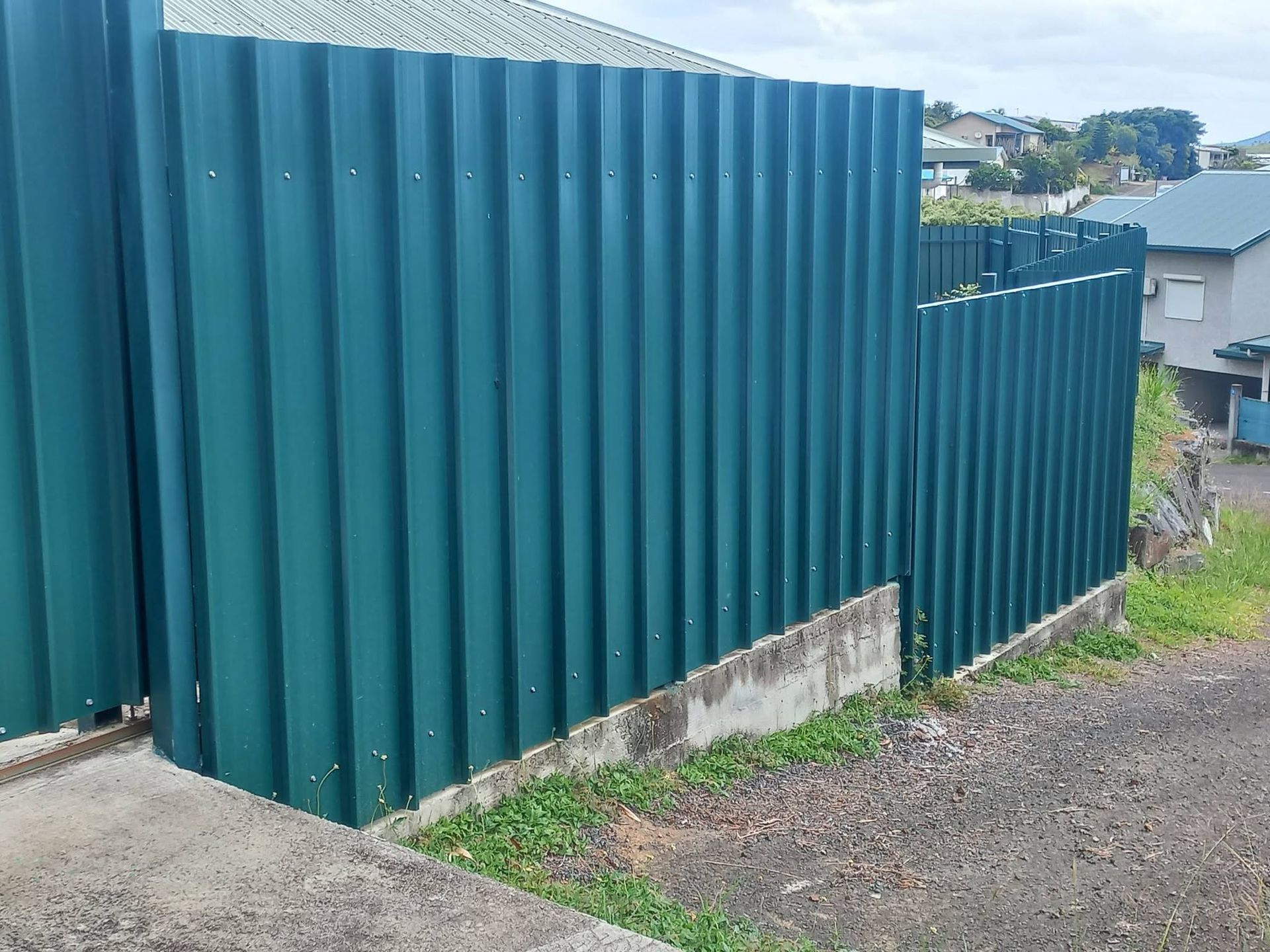 teal corrugated-metal fence panel along a driveway slope
