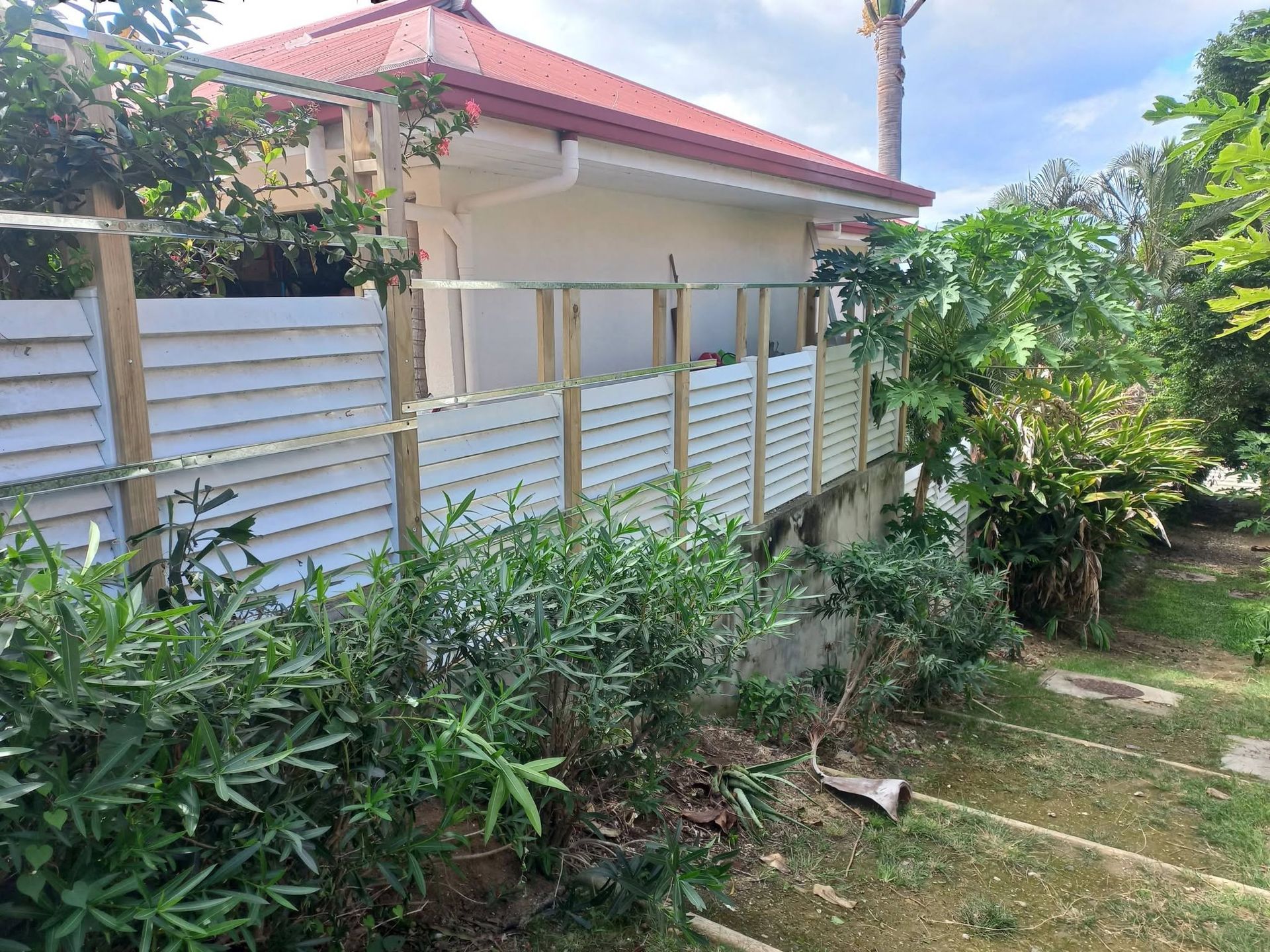 white/light panel fence bordering a garden, red-roofed house behind
