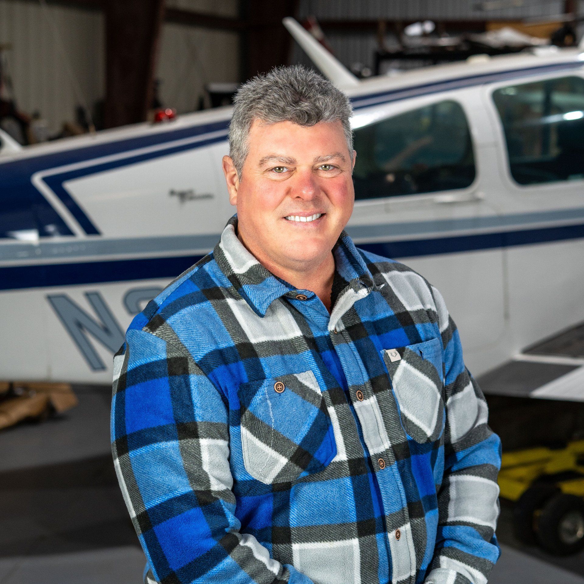 A man in a plaid shirt is standing in front of a plane with the letters ns on it