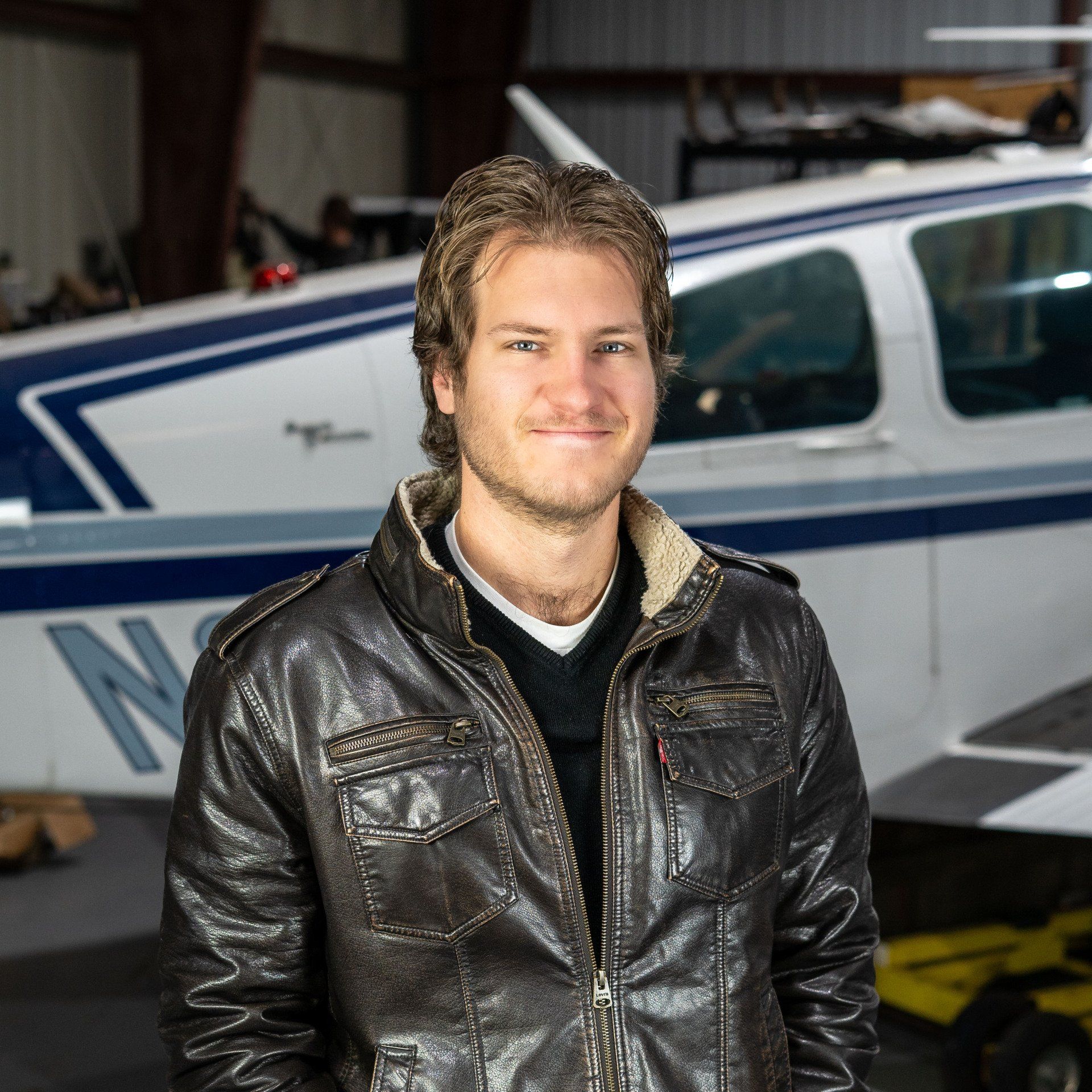 A man in a leather jacket stands in front of a plane with the letter n on it