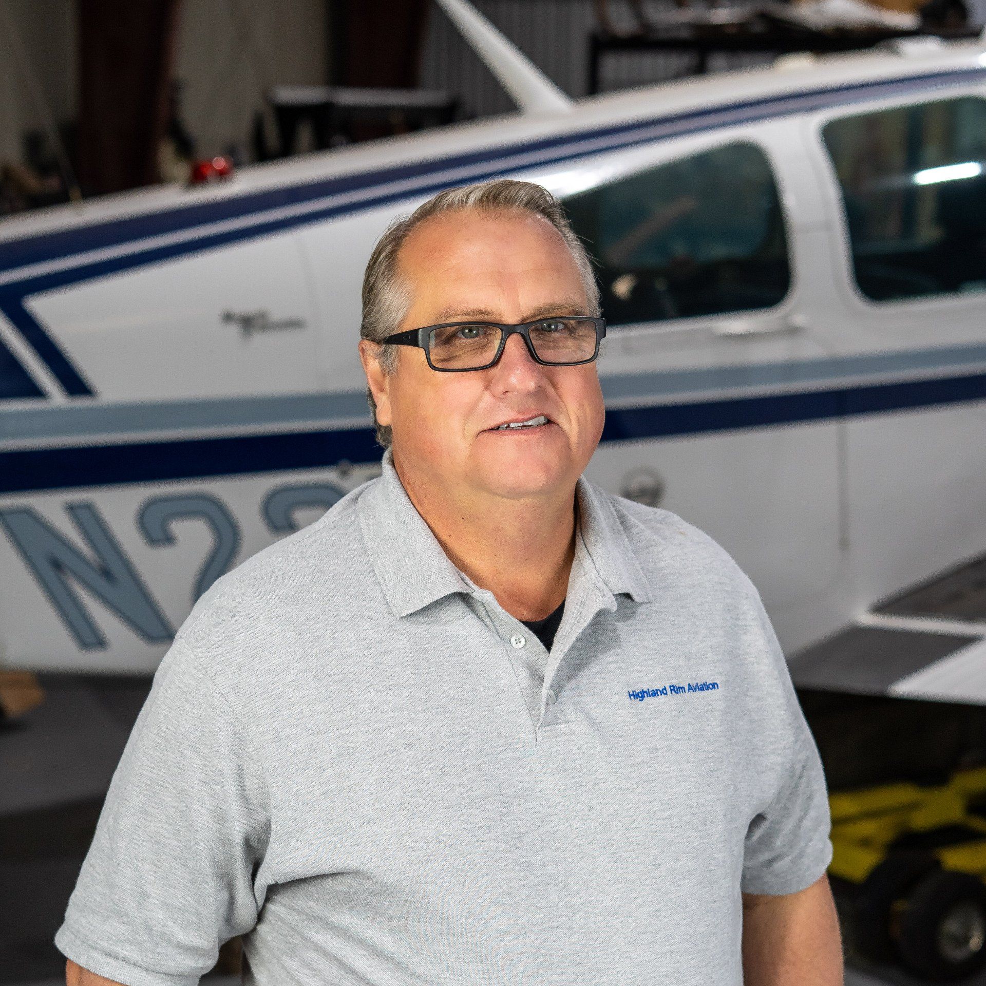 A man wearing glasses is standing in front of a small plane.