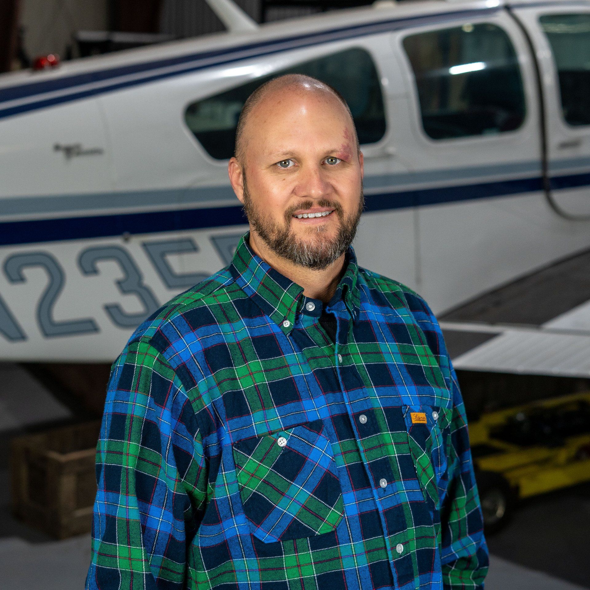 A man in a plaid shirt is standing in front of an airplane.