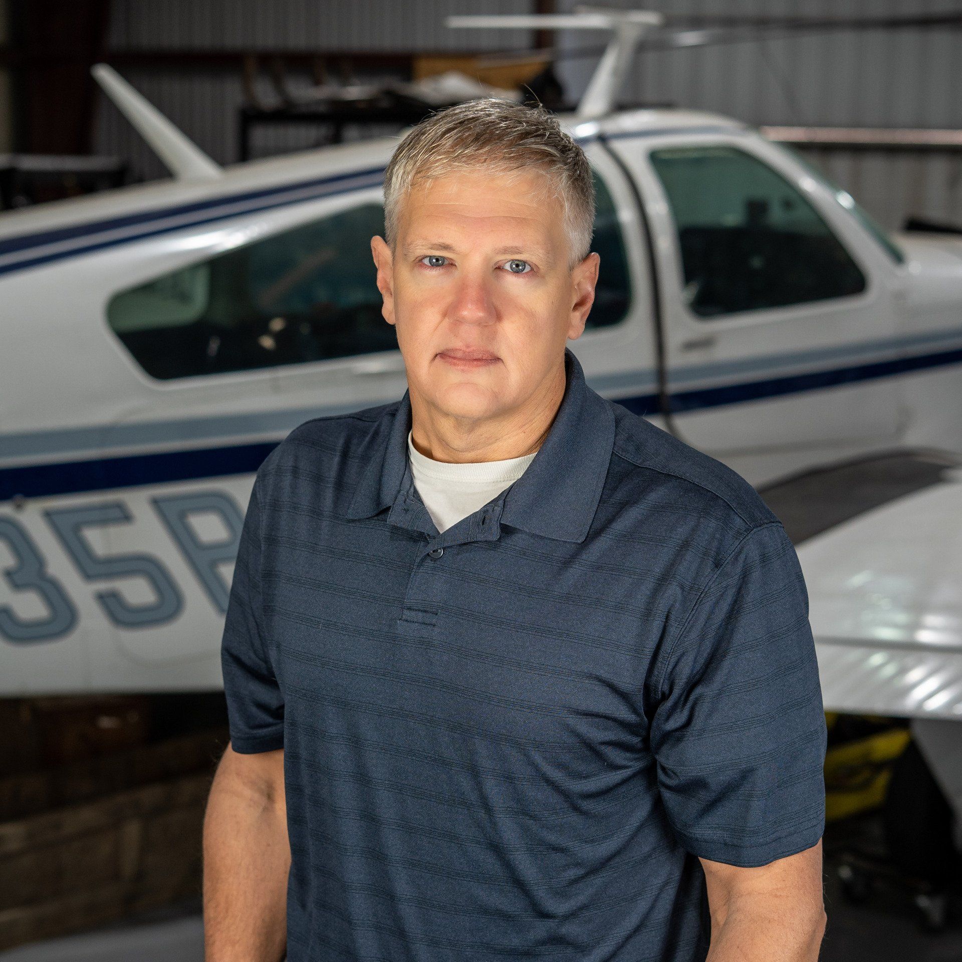 A man in a blue shirt is standing in front of a small plane.
