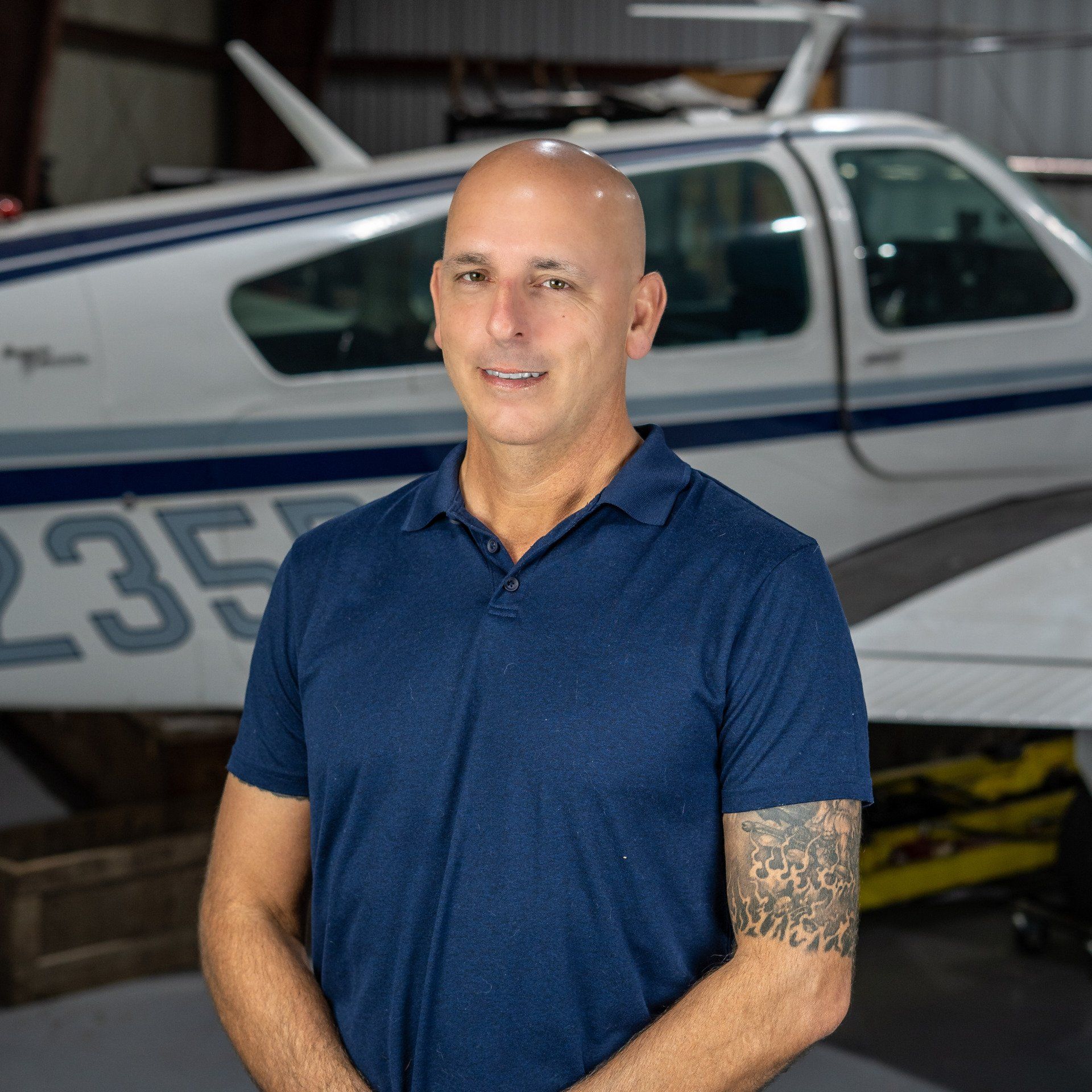 A man in a blue shirt is standing in front of a small plane.
