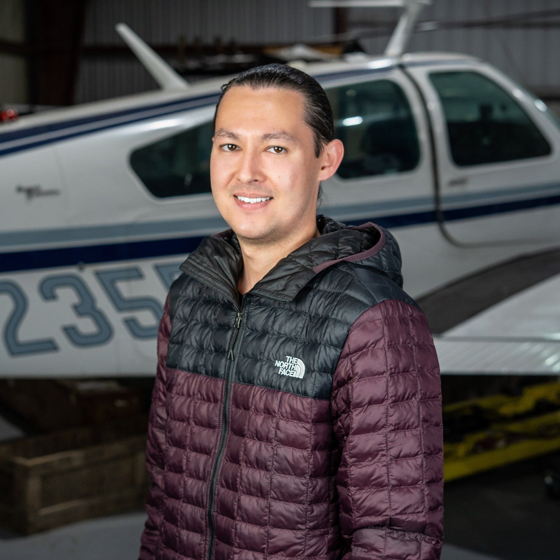 A man in a purple jacket is standing in front of a plane with the number 235 on it.