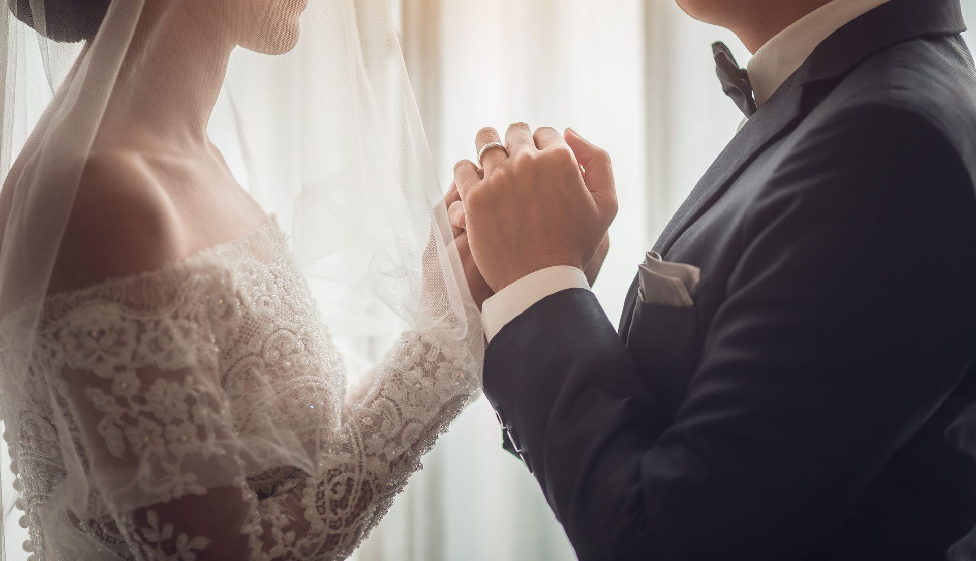 Bride and groom holding hands in a softly lit wedding moment by a window