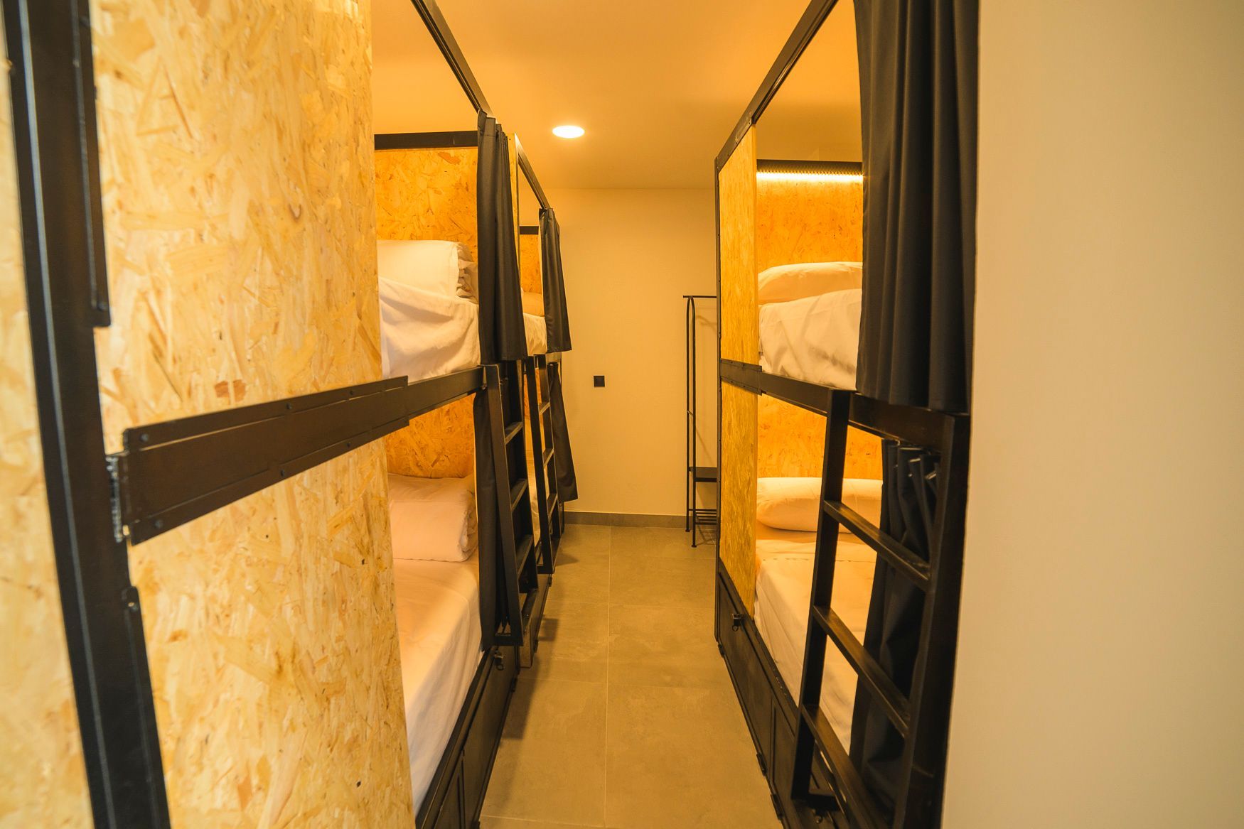 Pasillo estrecho del albergue con literas integradas en cubículos de madera.