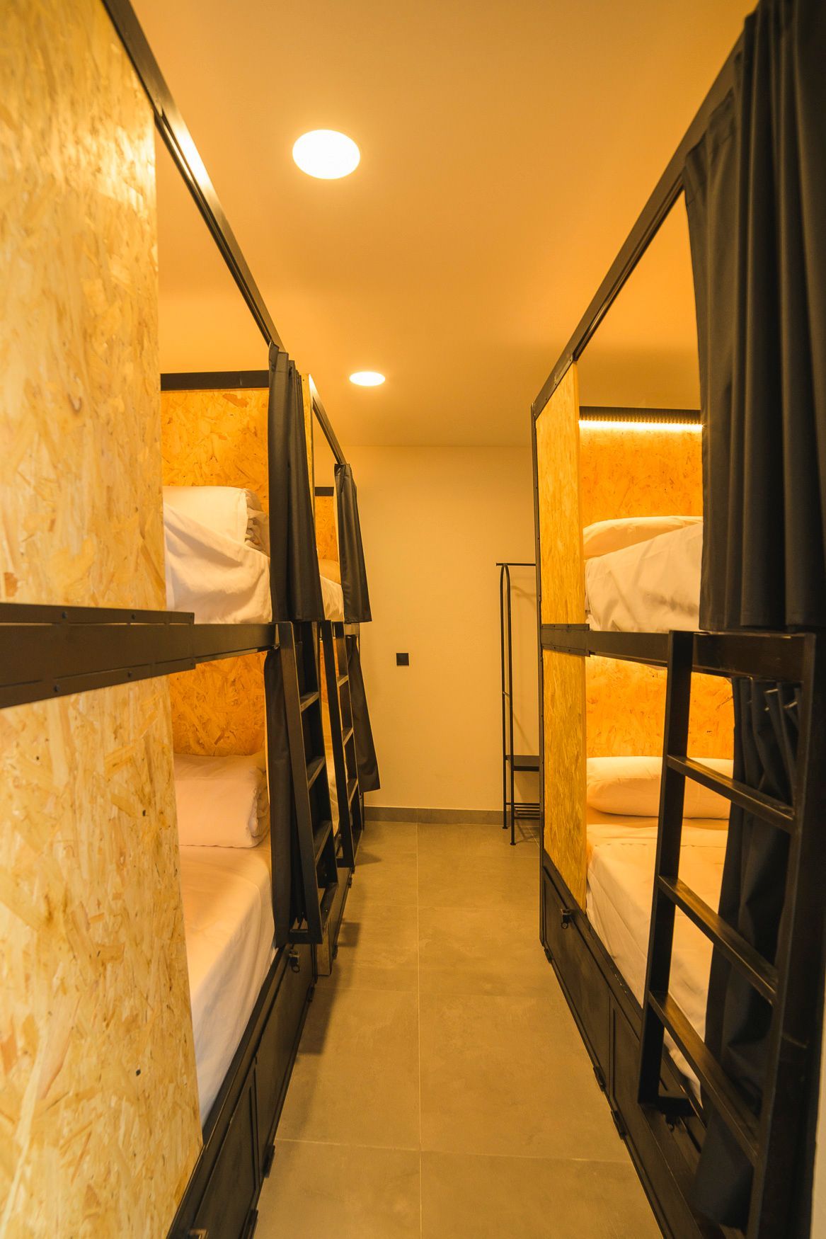 Habitación estrecha de albergue con literas; cada una con una cortina para mayor privacidad.