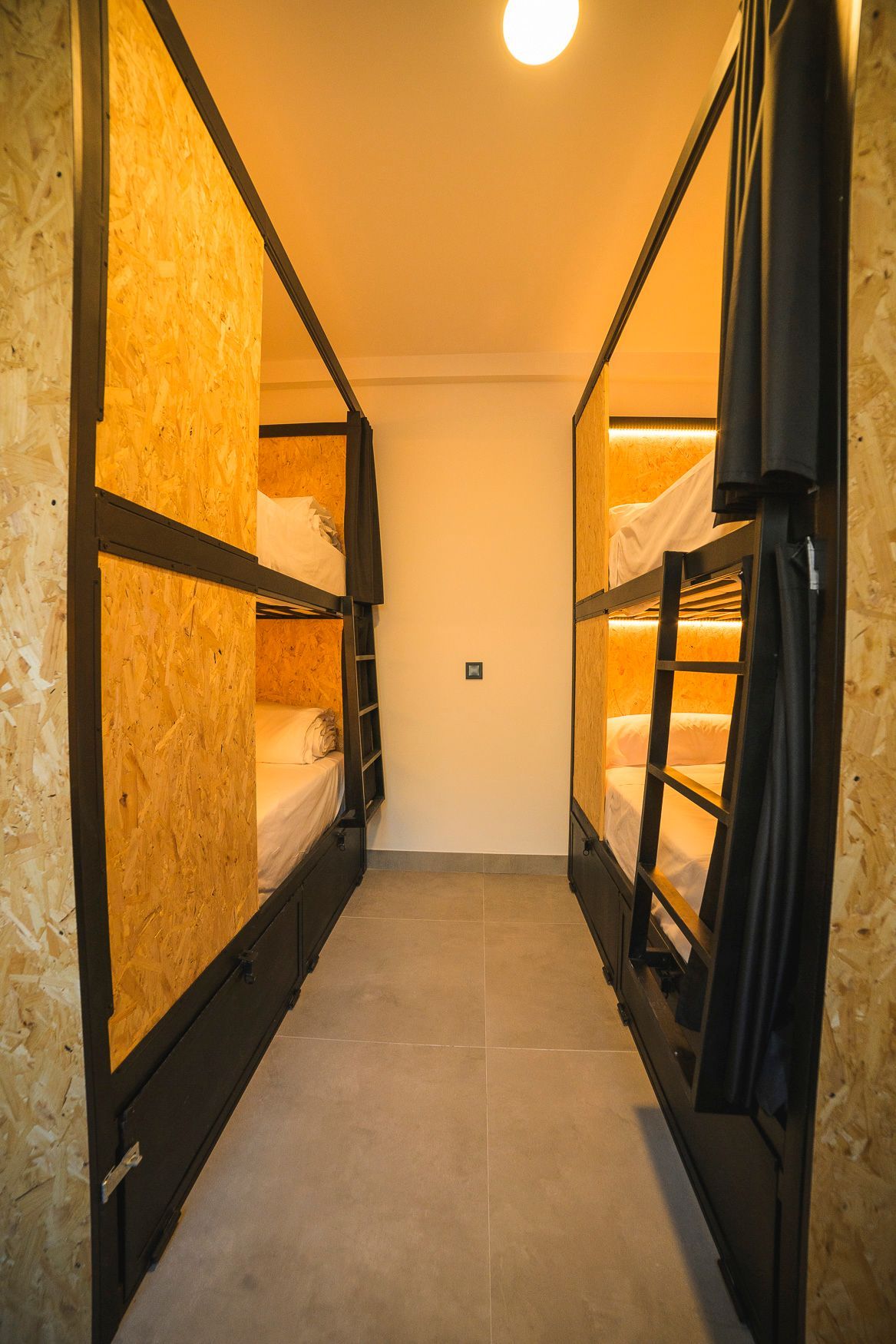 Dormitorio con literas y dos juegos de camas a lo largo de un pasillo estrecho; las camas tienen marcos de madera.