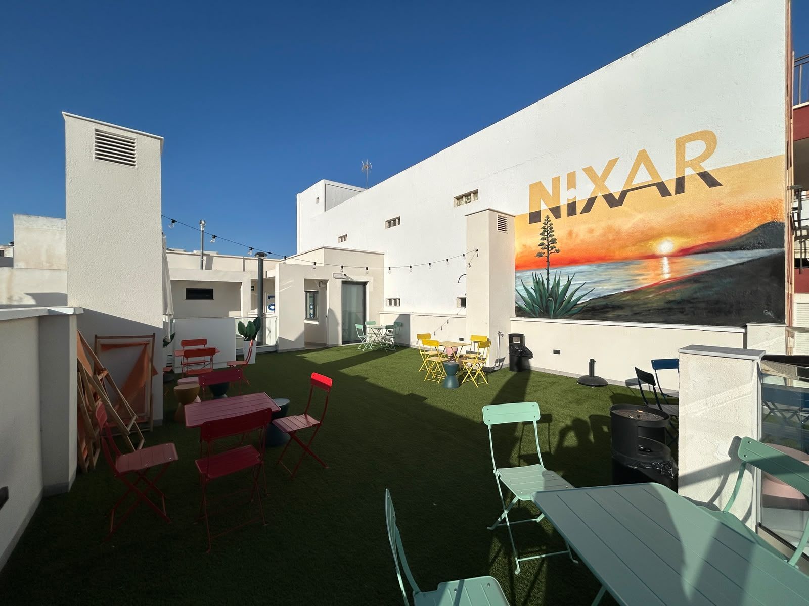 Terraza del Hostel Nixar en Almería con vistas a la Alcazaba, guirnaldas de luces y cesped.