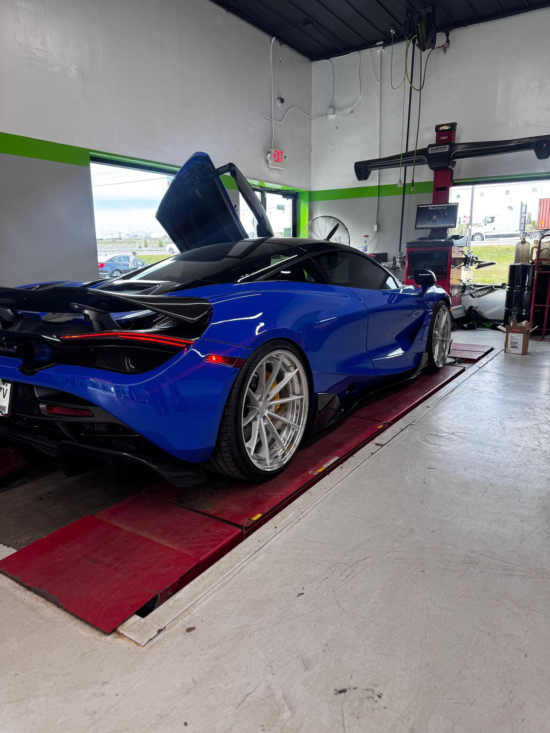 Blue McLaren sports car with open doors on a lift in a repair shop. | Honesty Automotive Repairs