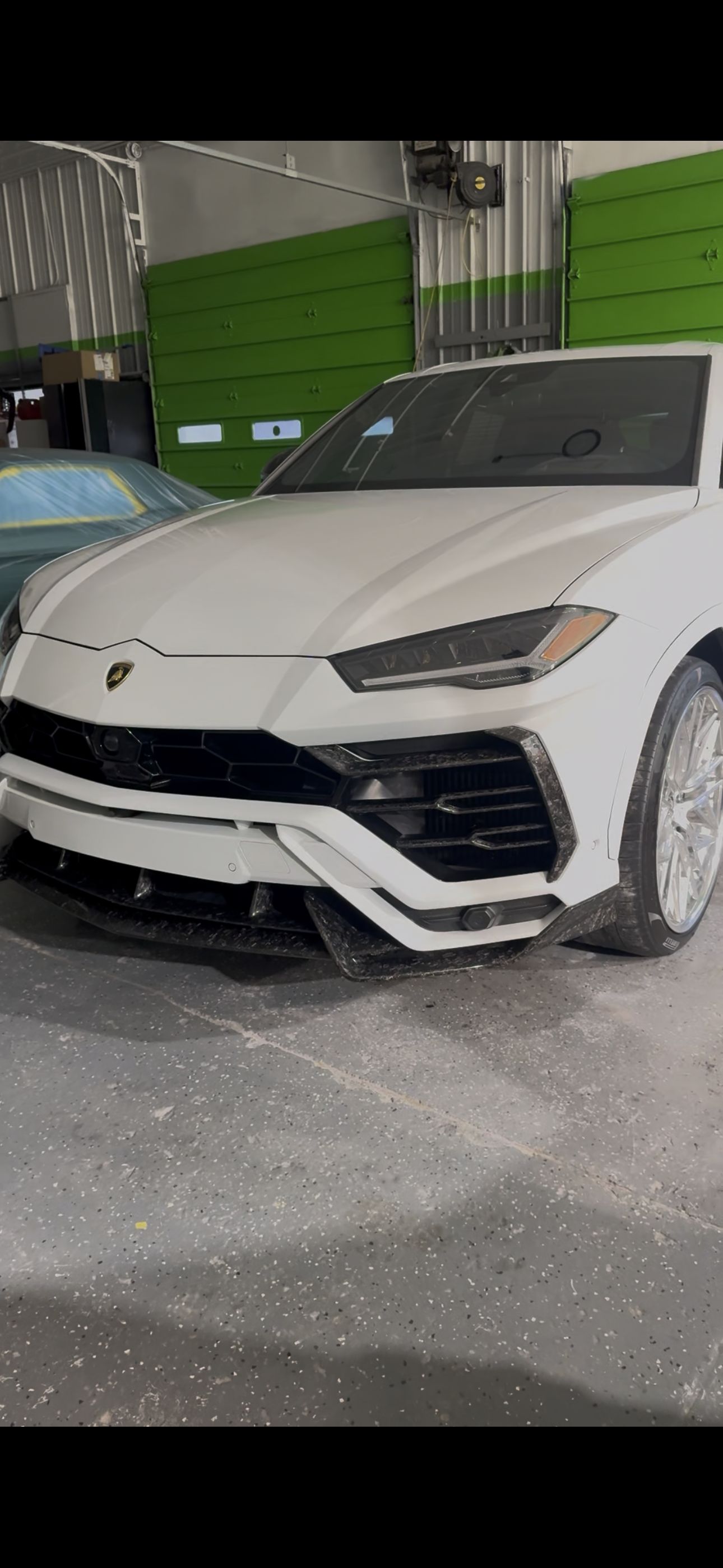 White Lamborghini Urus parked in a garage with green walls and gray floor. | Honesty Automotive Repairs