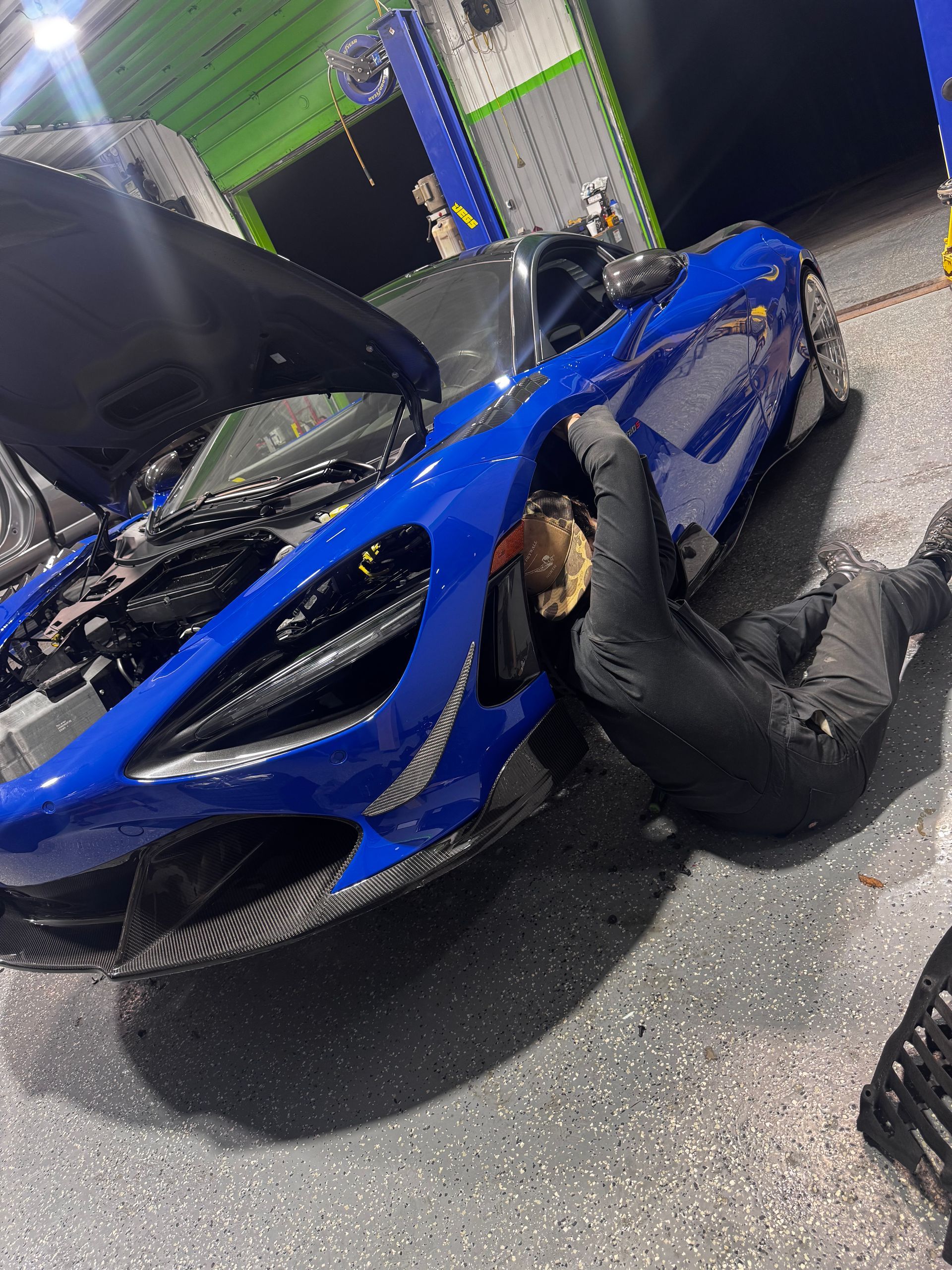 A person working on a blue sports car in a garage. Car's hood is open. Mechanic is on the ground. | Honesty Automotive Repairs