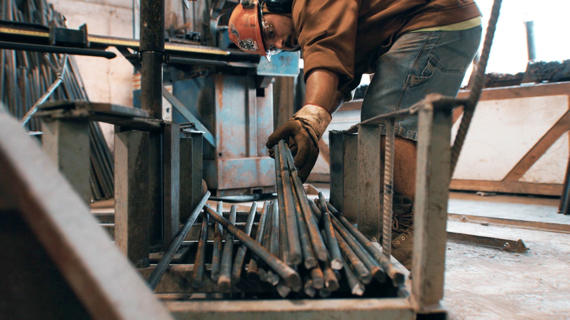 A man in a hard hat is working on a piece of metal in a factory.