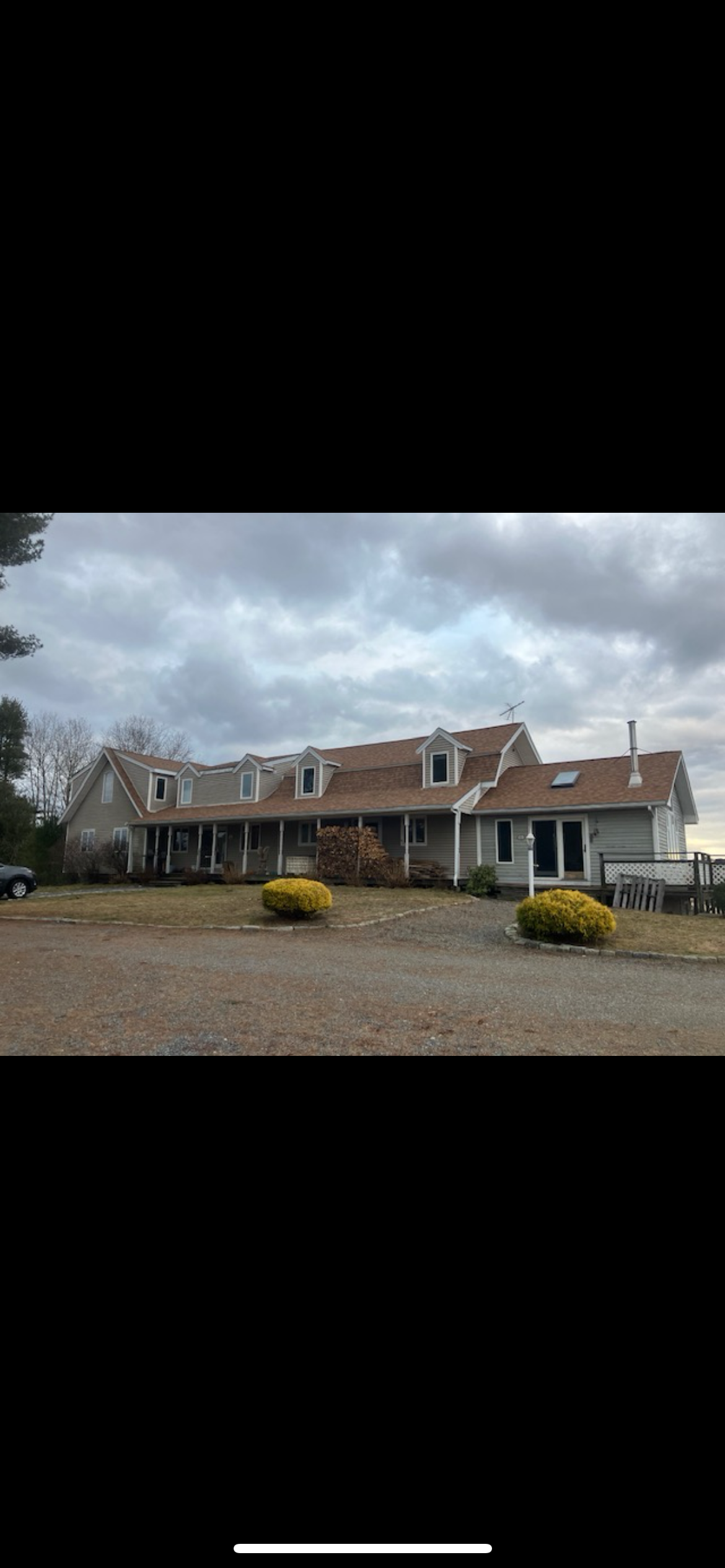 A large white house with a brown roof is sitting on top of a dirt field.