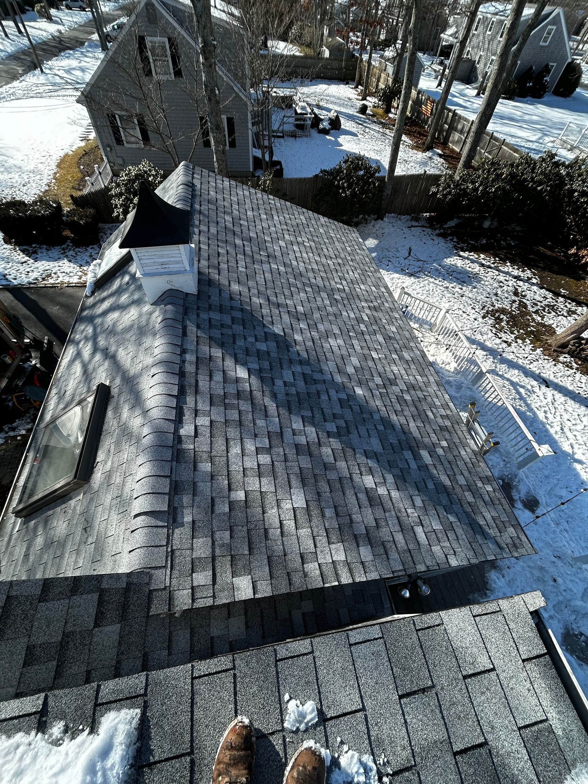 A person is standing on the roof of a house in the snow.