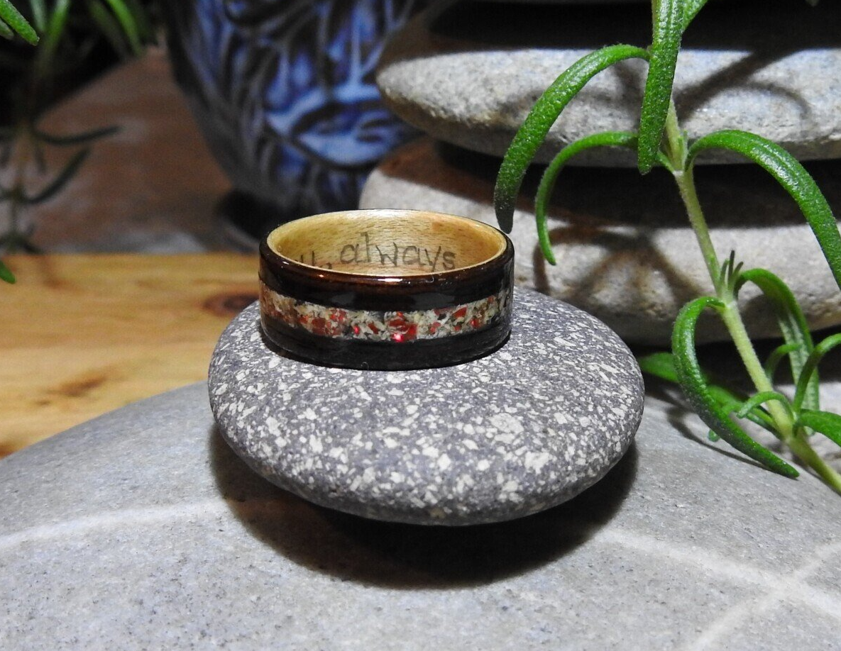 A Wooden Memorial Ring rests on a stone with a blue patterned pot behind it and a sprig of Rosemary beside it. 