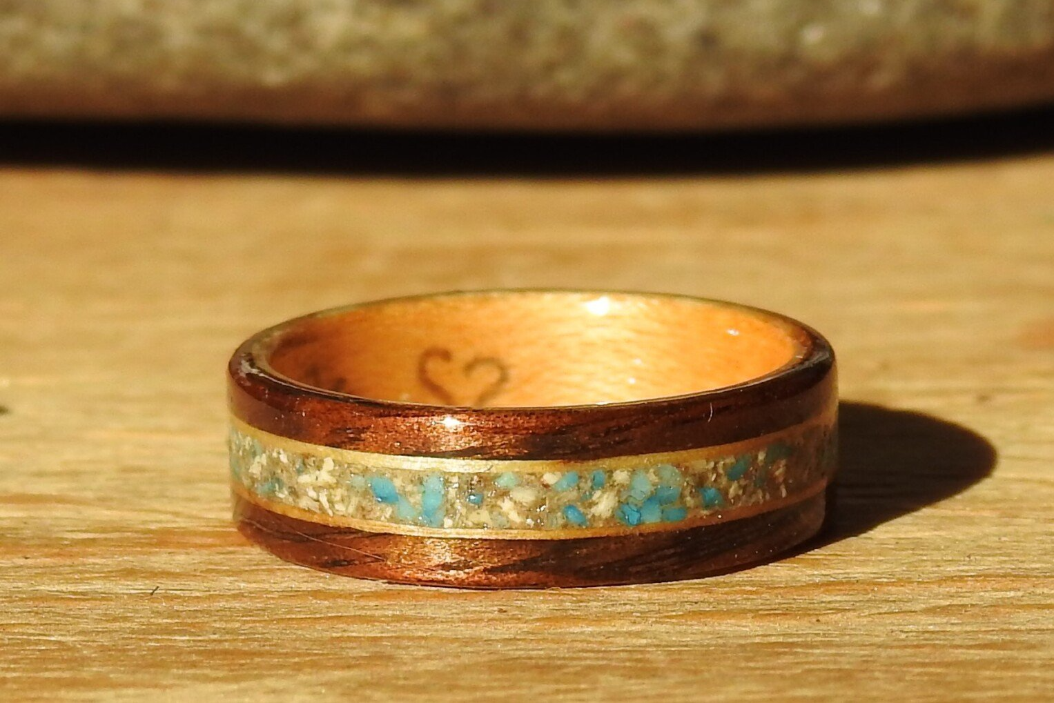 A wooden memorial ring with ashes and turquoise inlay rests on a wooden table.