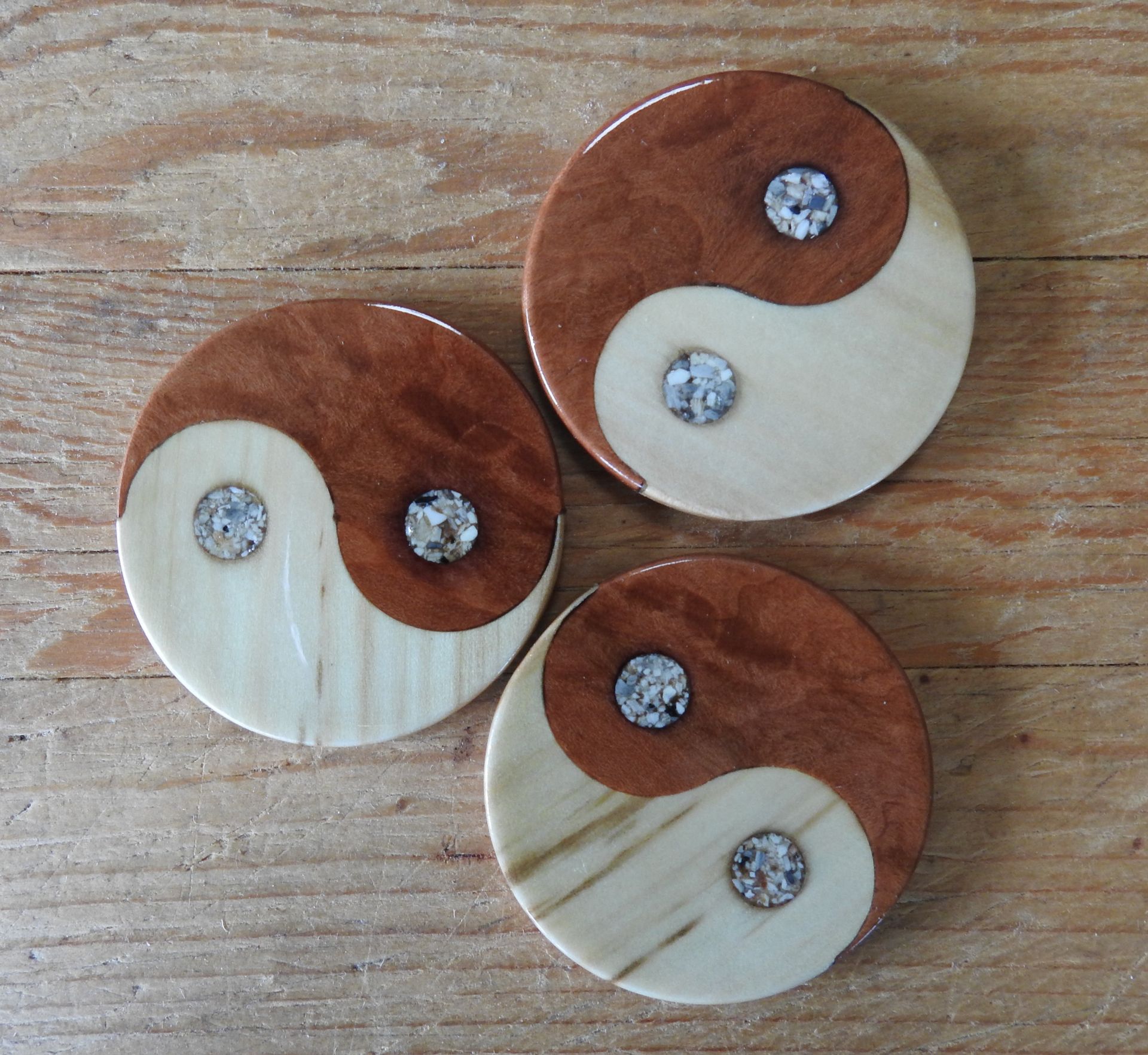 Three round yin-yang talismans of fir and juniper heartwood. The inlays are cremated ashes.
