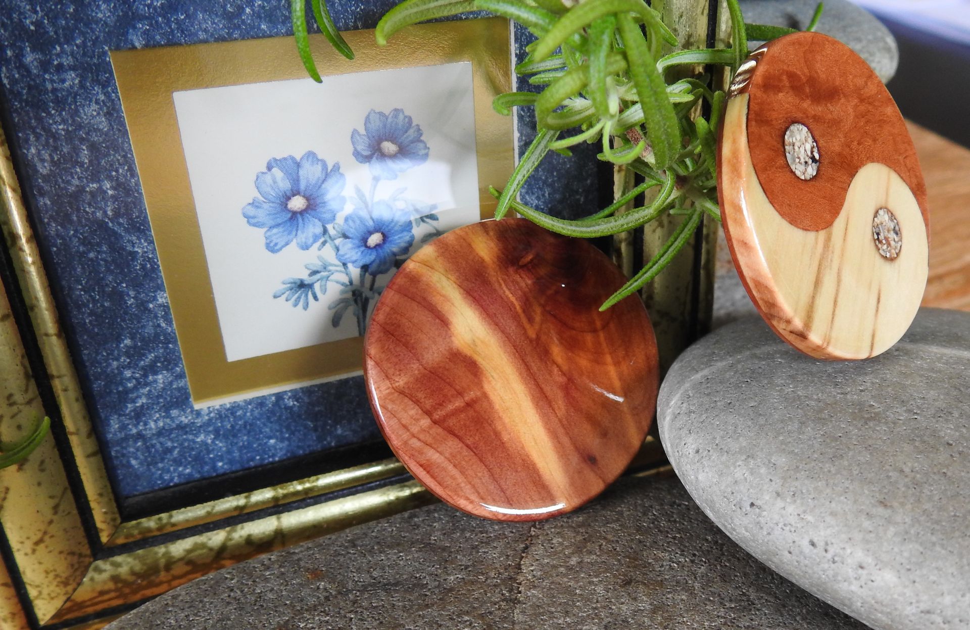 Two round talismans resting against a gold framed picture of small blue flowers, one talisman is resting on a stone.