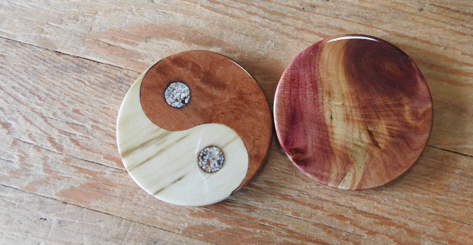 Two round wooden memorial talismans of Juniper heartwood and Fir. They lie flat on a wooden board. The talisman is inlaid with ashes. 
