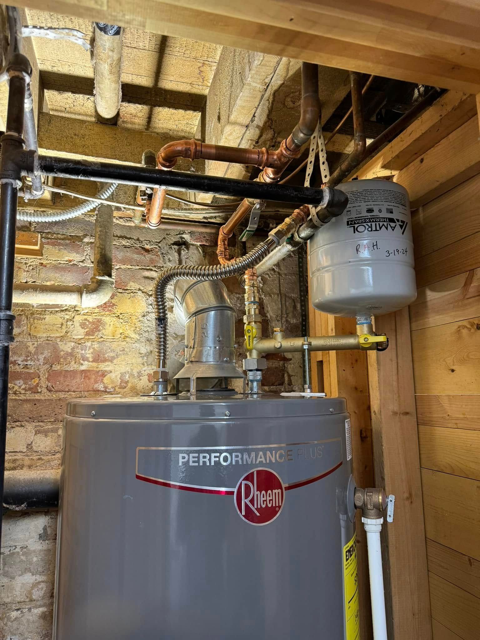 A Rheem Performance hot water heater, pipes, and expansion tank in a basement.