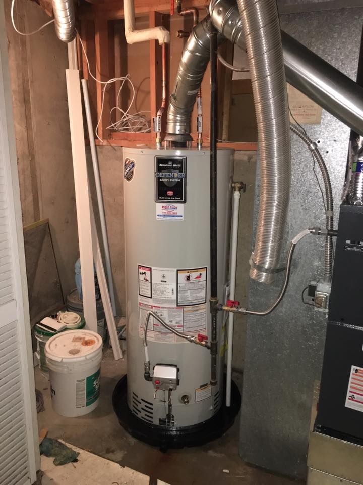 A tall, cylindrical water heater in a basement. It has connected pipes and is next to a furnace.