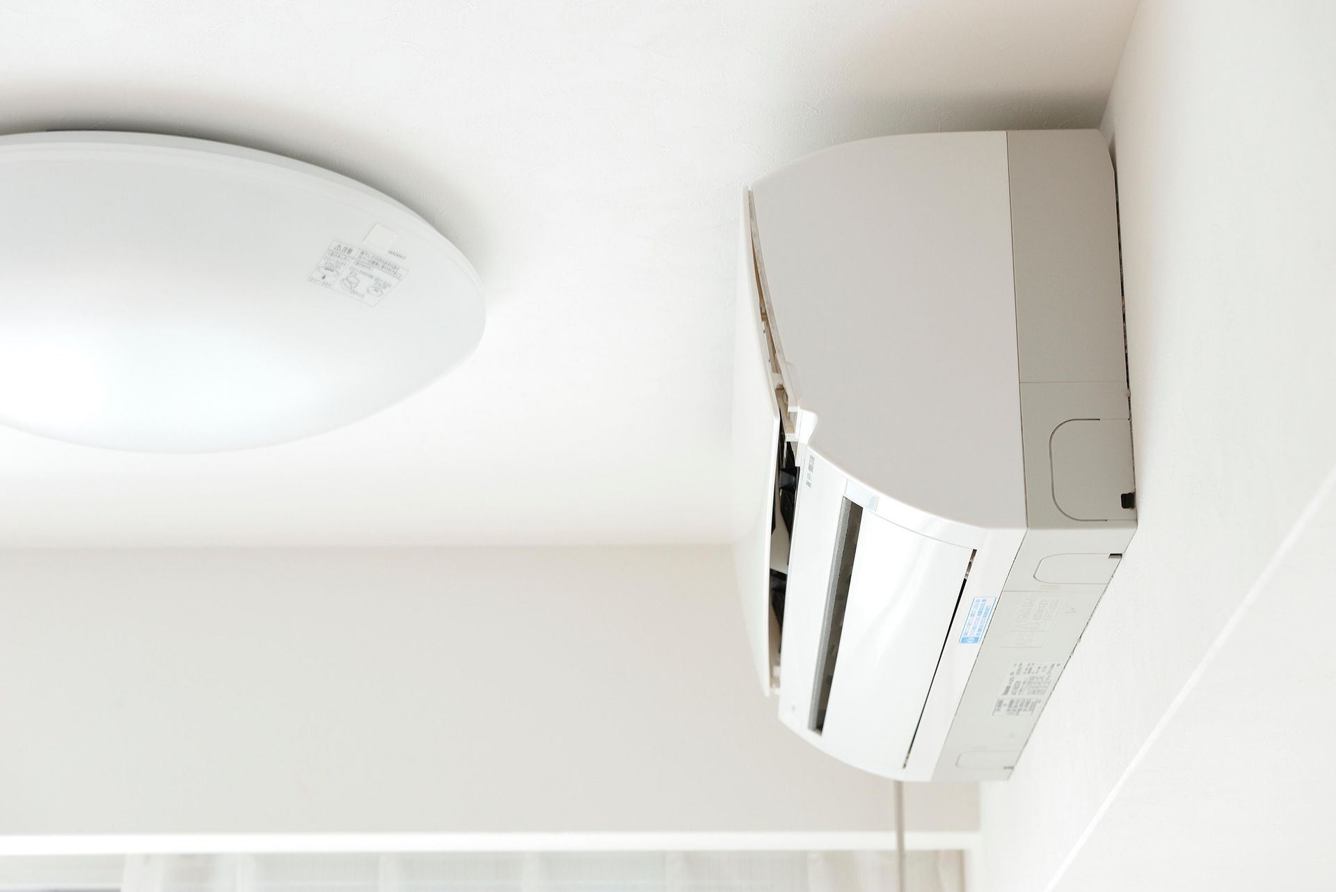White air conditioning unit mounted on a white wall, next to a white ceiling light.