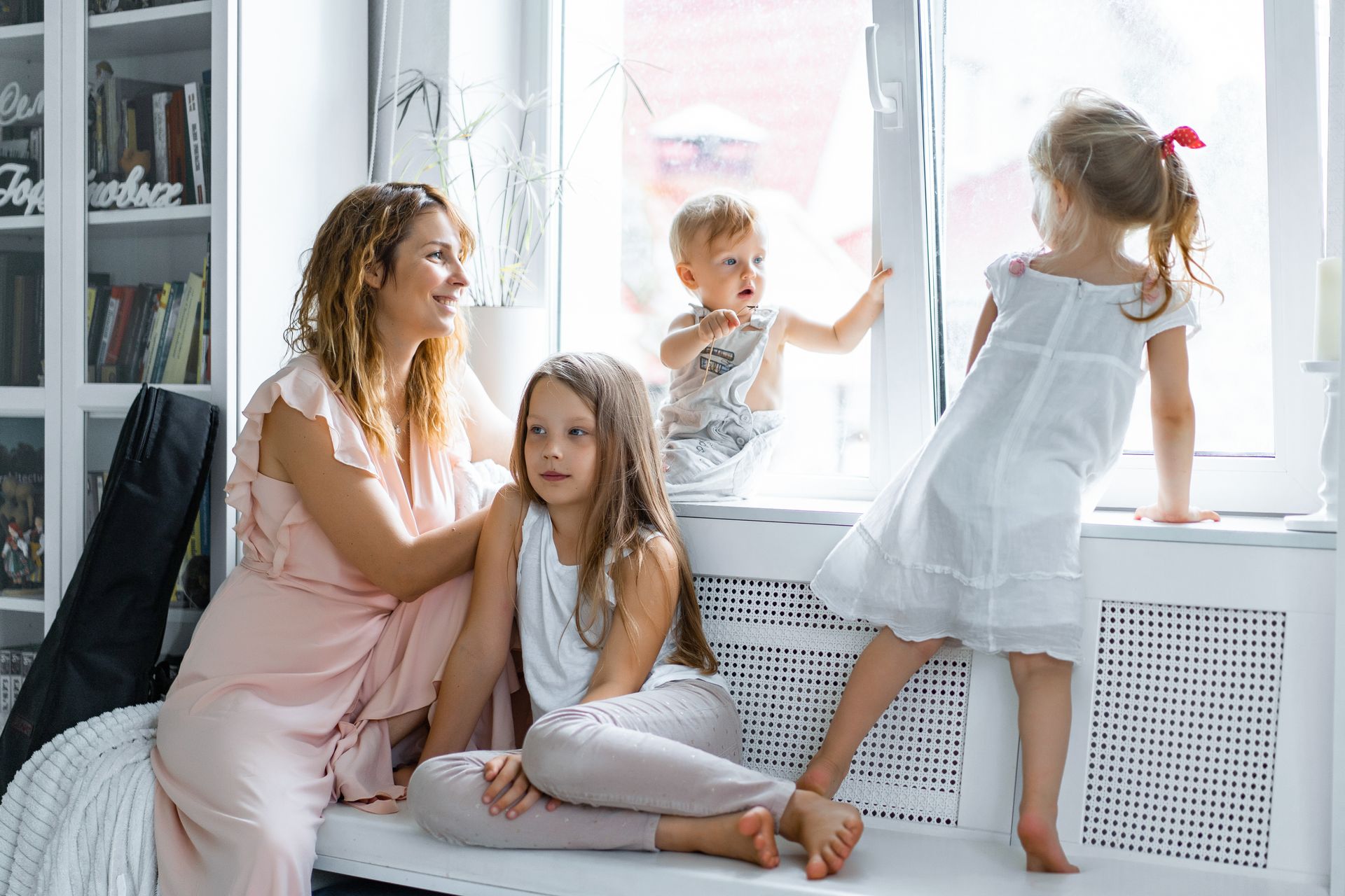 Woman with three children by a window; smiling and looking out.