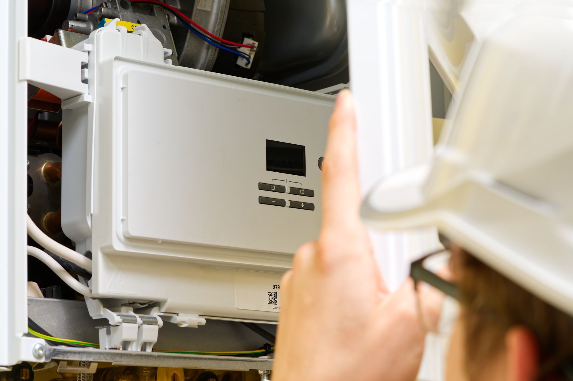 Person in a hard hat points at a white heating system component.