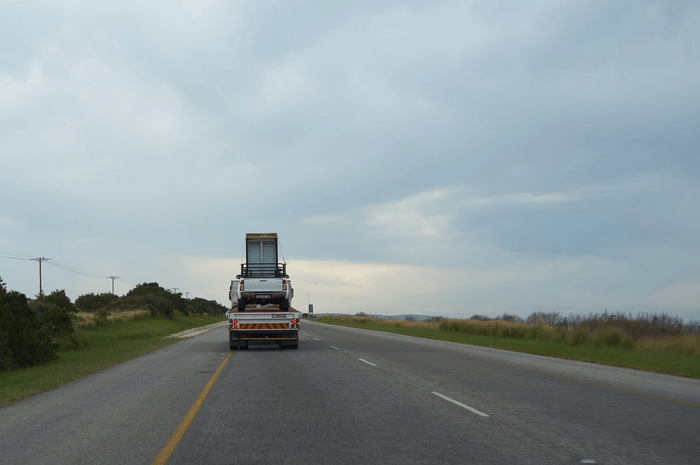 Truck carrying a stacked load of white structures on a highway under a cloudy sky.