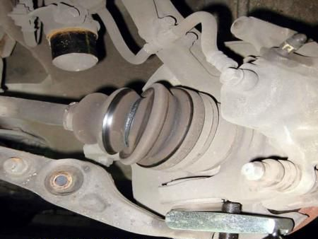 Close-up of a car’s CV axle and torn rubber boot under the wheel well
