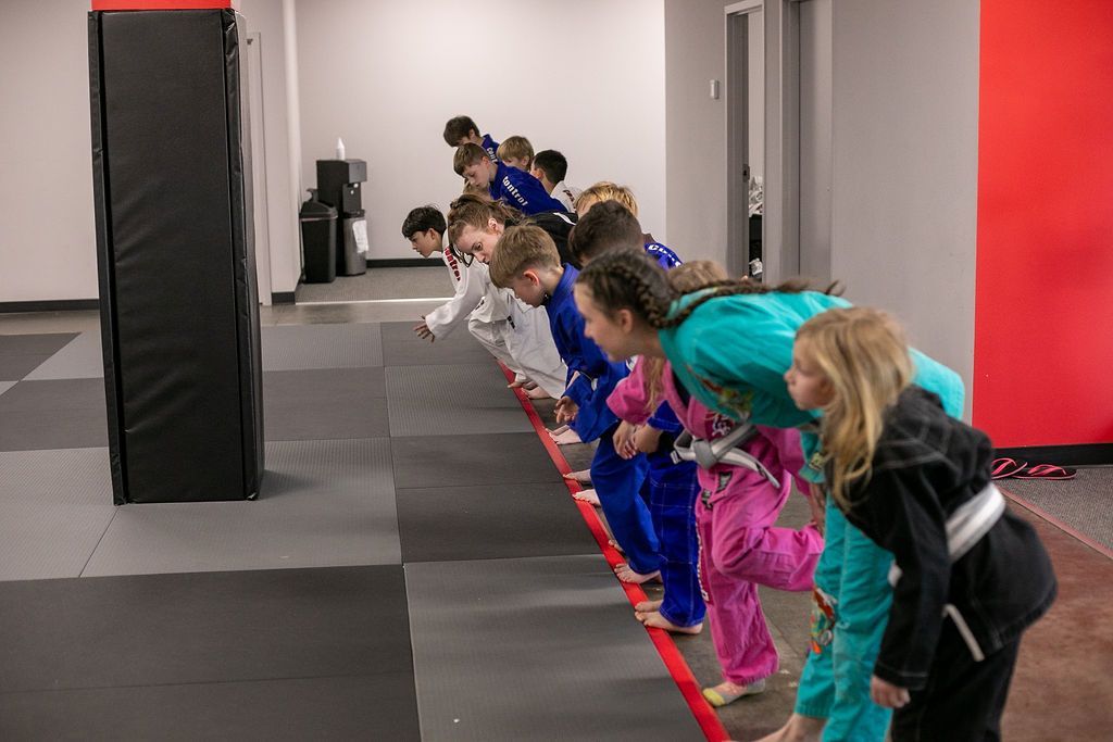 Children leaning forward in a line during an indoor obstacle course, facing a padded wall
