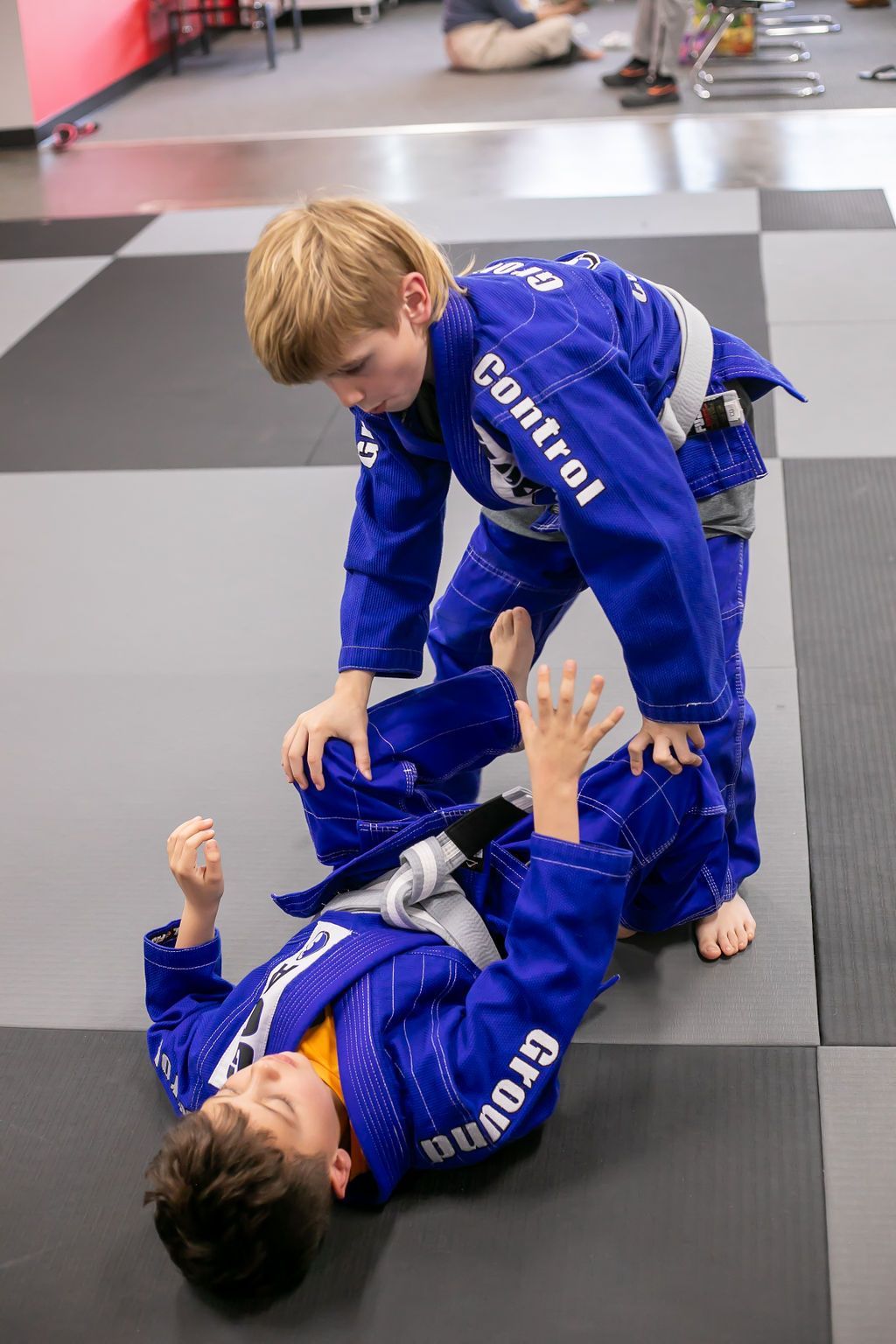 Two children in blue martial arts gis practicing grappling on padded gym mats