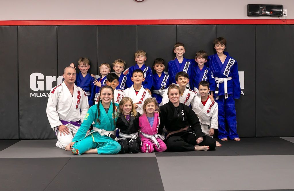 Martial arts team posing on mats in a gym, wearing blue, white, green, pink, and black uniforms