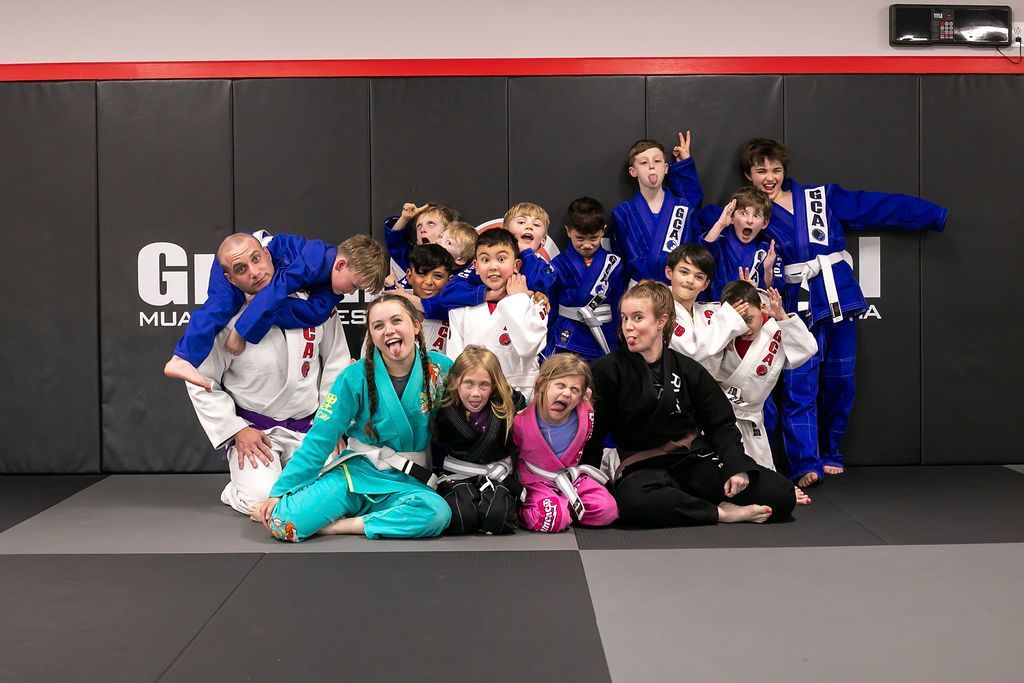 Group of kids in blue and teal martial arts uniforms posing on a gym mat