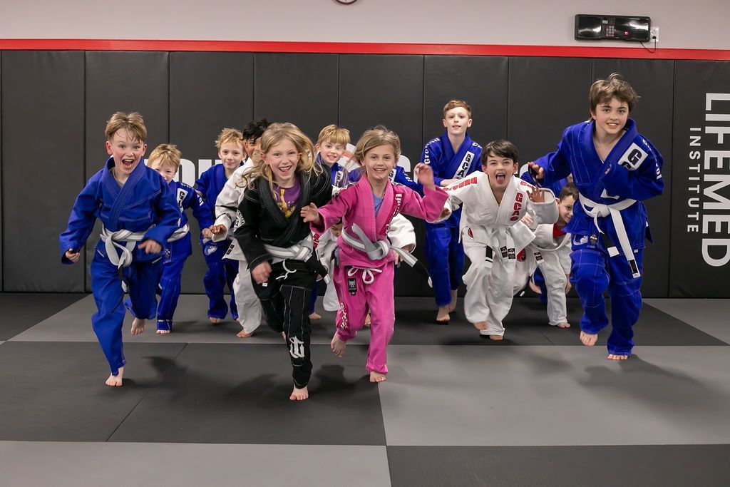 Children in colorful martial arts uniforms run toward the camera in a training gym.