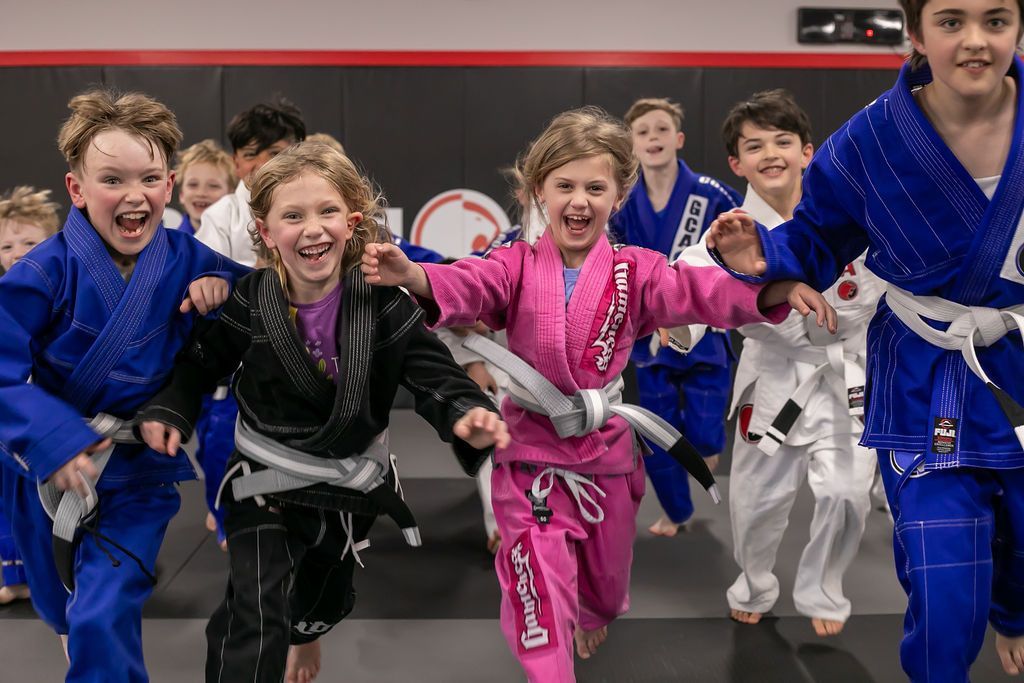 Children in colorful martial arts uniforms running toward the camera in a dojo
